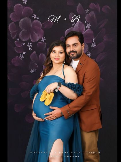 A classic studio portrait with a floral background. The couple holds a pair of yellow baby shoes, adding a sweet pop of color and anticipation to their maternity photo.
