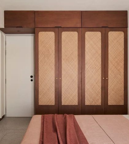 The 'dusty rose bedroom' is designed with a 'less is more' philosophy. The custom wardrobe with woven panel doors and the simple bed frame create a space that is serene and uncluttered.