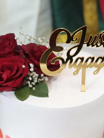 A detailed shot of the "Just Engaged" topper on a cake decorated with fresh red roses and baby's breath.