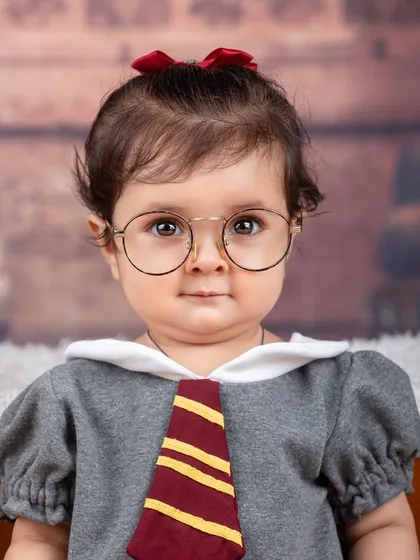 A close-up portrait of a baby girl dressed as a Hogwarts student, looking thoughtful and sweet.