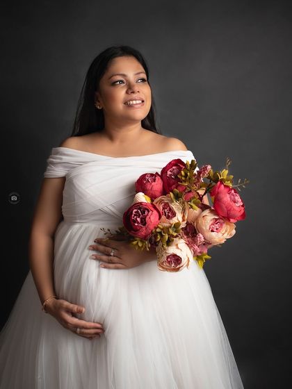 A classic studio portrait. The mother-to-be in a white gown holds a vibrant bouquet, her happy expression lit by the studio lights.