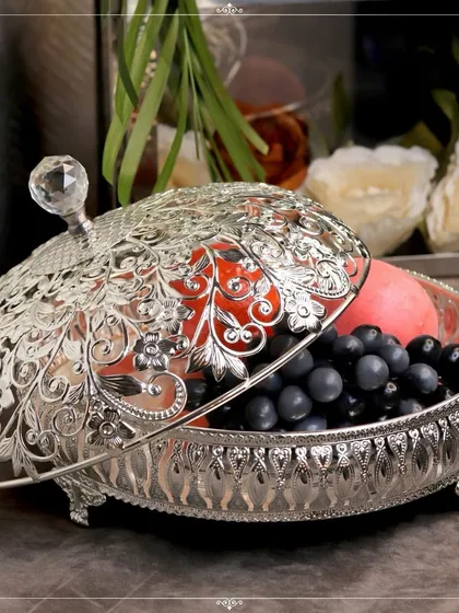 This ornate silver-plated fruit bowl with a lid is a stunning centerpiece for any dining table. The intricate floral cutout design on the lid is simply breathtaking.