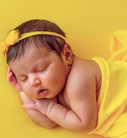 A simple and sunny portrait with a bright yellow wrap and background. This classic side-lying pose is perfect for capturing the baby's profile and chubby cheeks.