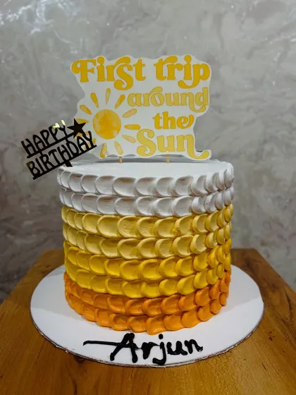 A "First trip around the Sun" themed cake with a warm yellow and orange ombre petal effect, perfect for a first birthday.