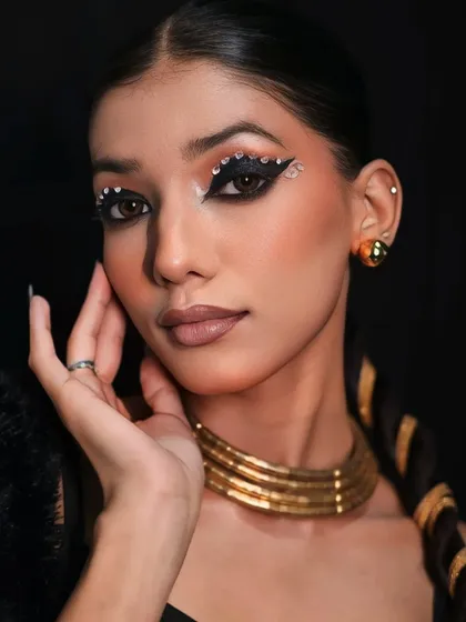 A close-up on a glamorous, creative makeup look, featuring bold, bejeweled eyeliner and a sleek, braided hairstyle.