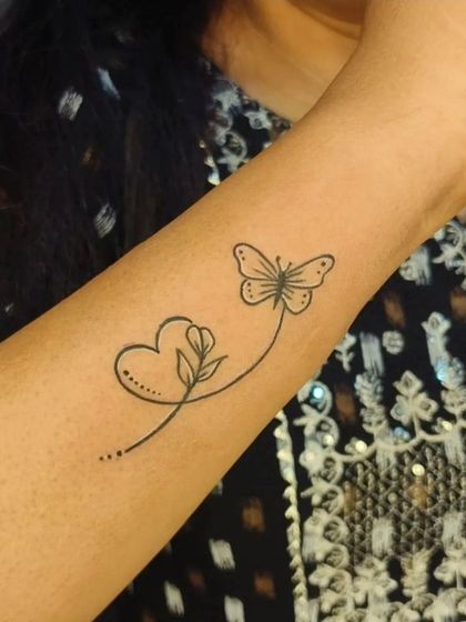 This fine-line tattoo combines a heart, a flower, and a butterfly into one continuous line. It's a beautiful and creative design that flows gracefully on the arm.