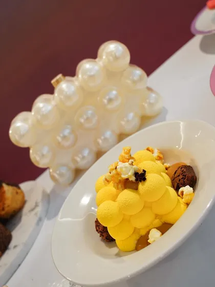 A yellow, bubble-shaped dessert next to a pearl-encrusted clutch at the Ajio Luxe Café. This pairing highlights how our food is designed to be as stylish as the fashion it accompanies.
