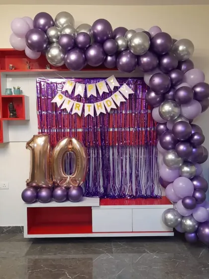 A balloon arch in purple and silver framing a TV unit for a 10th birthday celebration at home.