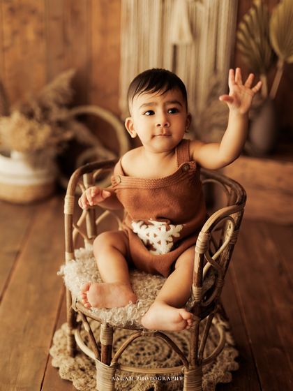 A cute little wave from this baby sitting in a miniature rattan chair.