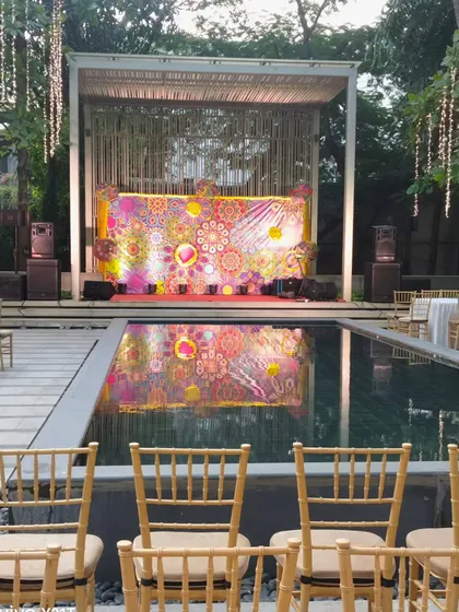 The stage for a poolside event, featuring a vibrant and colorful backdrop that is beautifully reflected in the water. This setup is perfect for a lively Sangeet or Mehendi party.