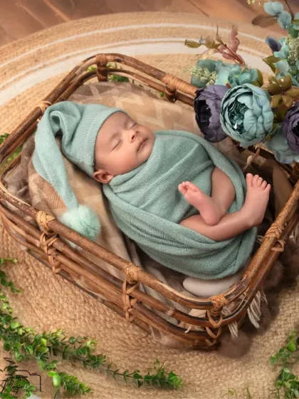 A beautiful newborn wrapped in a mint green swaddle, sleeping peacefully in a rustic basket surrounded by flowers.