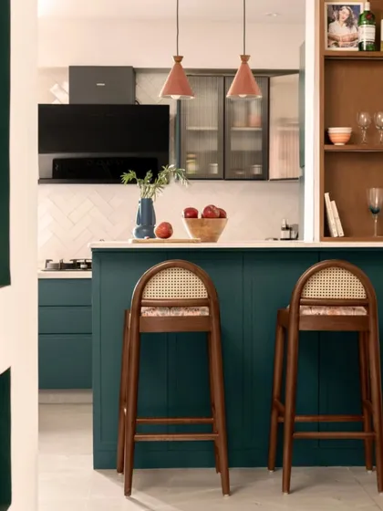 The kitchen is designed around a functional island that doubles as a breakfast bar. I chose a deep teal for the cabinetry and paired it with warm wood bar stools and terracotta pendant lights for a rich, layered look.