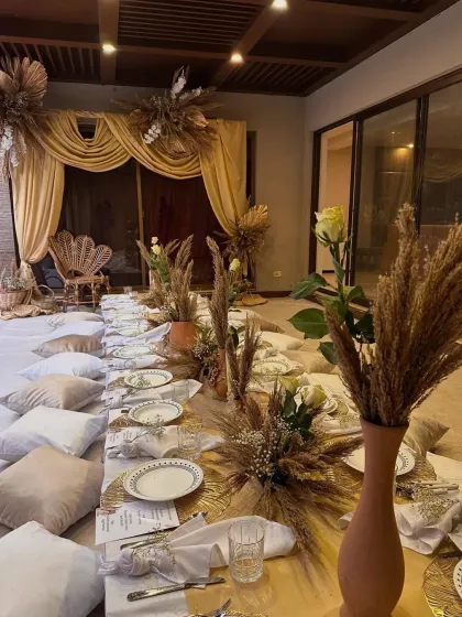 An intimate and chic boho-style gathering perfect for a relaxed celebration. This setup features low picnic tables, plush floor cushions, and earthy decor with pampas grass, creating a warm and inviting atmosphere for guests to connect and enjoy.