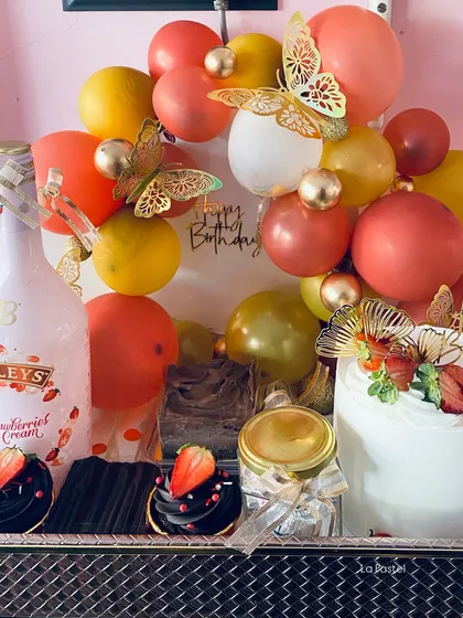 A close-up of my deluxe birthday hamper, showing the strawberry cream liqueur, chocolate cupcakes, and a custom cake with a balloon backdrop.