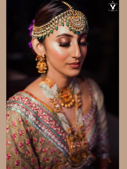 A close-up portrait focusing on the bride's exquisite matha patti and flawless makeup. The warm lighting and her serene expression create a look of timeless elegance.