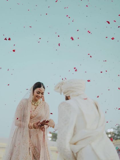 A beautiful, minimalist shot of the varmala exchange against a pale blue sky. The shower of red petals adds a pop of color to this serene and elegant moment.