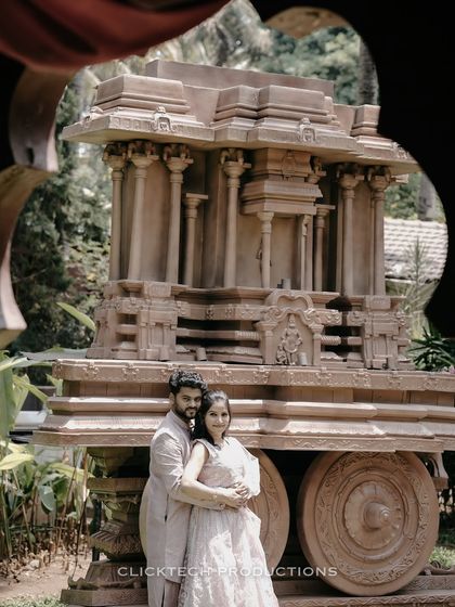 A creatively framed shot of a couple posing in front of a temple chariot replica, viewed through a decorative opening.