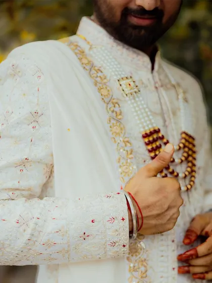 A detailed shot focusing on the groom's embroidered sherwani and traditional pearl necklace. This close-up captures the fine craftsmanship of his wedding day attire.