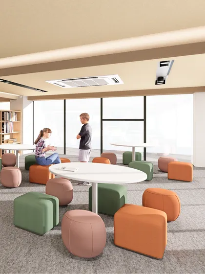 An informal collaboration zone within a library, featuring low tables and colorful ottomans. We design libraries with flexible layouts that can shift as needs evolve, allowing for both quiet pause and active group work.