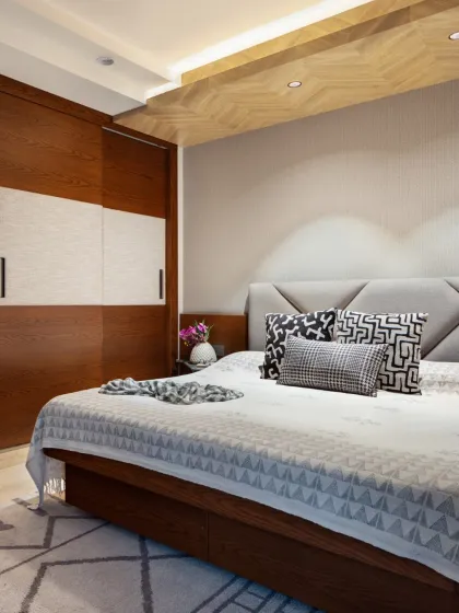 The master bedroom at Rue 32 redefines serenity with a refined palette of greys and natural wood. A commanding bed with a grey upholstered headboard sits beneath a herringbone wooden ceiling, creating a soulful sanctuary for quiet moments.