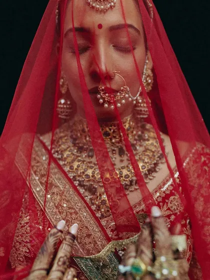 A quiet moment of reflection for the bride, Rakhi, enveloped in her vibrant red veil. I focus on capturing the profound emotion and intricate details that define your wedding day.