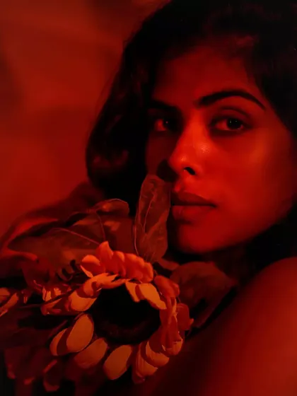 A captivating close-up where her eyes speak volumes. The sunflower frames her face, and the red light adds an intense, emotional charge.