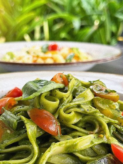 A close-up of our vibrant green pesto fettuccine, tossed with cherry tomatoes and fresh basil.