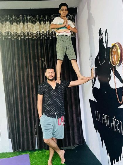 A proud father-son moment. I'm balancing in a tree pose while my son stands on my shoulder, showing strength and connection.