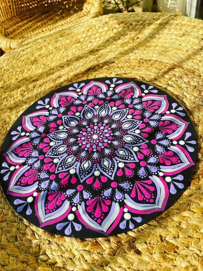 A finished pink and purple dot mandala resting on a woven jute surface, highlighting its rich colors and textures.