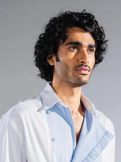 Men's grooming for an editorial shoot, focusing on enhancing the model's natural curly hair texture. The skin is perfected for a matte, even finish under studio lighting.