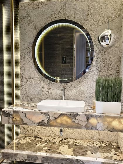A powder room featuring a backlit Patagonia marble vanity. The round mirror with integrated lighting and the dark accent wall create a moody and sophisticated atmosphere.