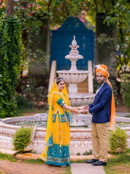 A couple in traditional Rajasthani attire by a beautiful white fountain, creating a royal and elegant scene.