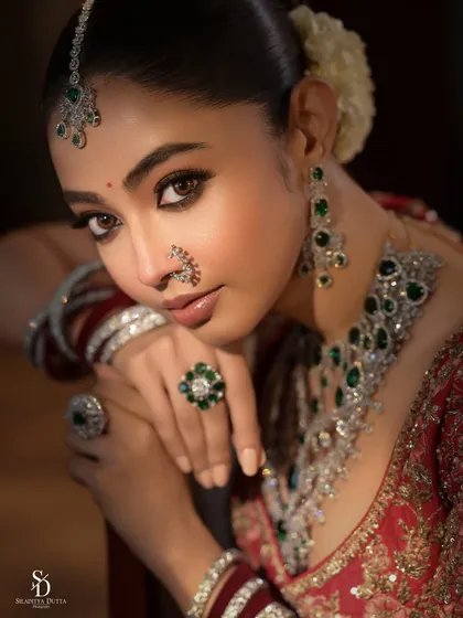 A close-up bridal portrait that focuses on emotion and detail. The soft lighting highlights the intricate diamond and emerald jewellery, the delicate makeup, and the serene expression of the bride, capturing a quiet moment of beauty.