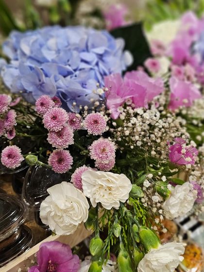 A close-up of the stunning floral arrangements from a grand 70th birthday hamper. The mix of blue hydrangeas, pink button mums, and white carnations creates a beautiful, celebratory feel.