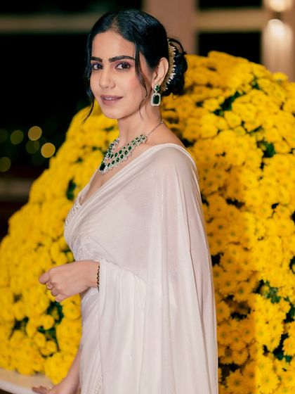 A close-up showing the elegant hairstyle and emerald jewelry, perfectly complementing the white saree and the resort's vibe.