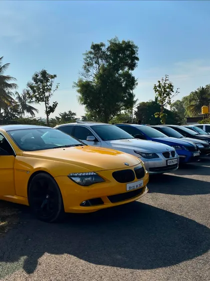 A row of beautiful cars, led by a yellow BMW coupe, lined up during a sunny morning meet.