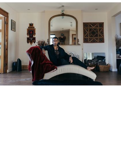 A wide environmental portrait of Nilikkhimani in his living space, showcasing his connection to his personal surroundings.