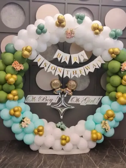 A 'Baby is on the way' gender reveal party setup with a circular balloon arch in green, blue, and white.