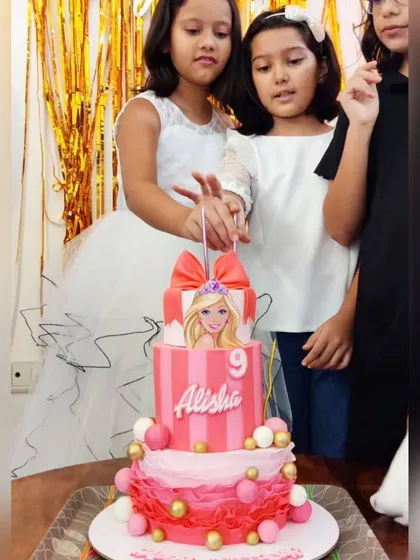 Alisha celebrating her 9th birthday with a three-tier Barbie cake. The design features pink stripes, ruffles, and a beautiful Barbie topper.