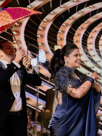 A playful moment from a parents' performance, using a colorful umbrella as a prop to recreate a classic Bollywood scene.