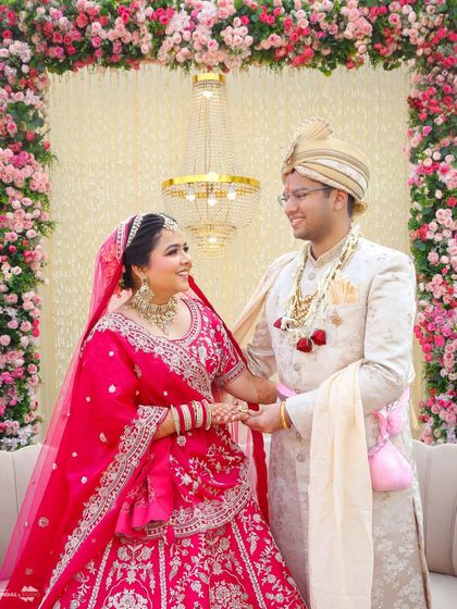 A sweet moment between the couple, framed by a stunning floral arch. Their happy expressions and coordinated outfits make for a perfect wedding portrait.