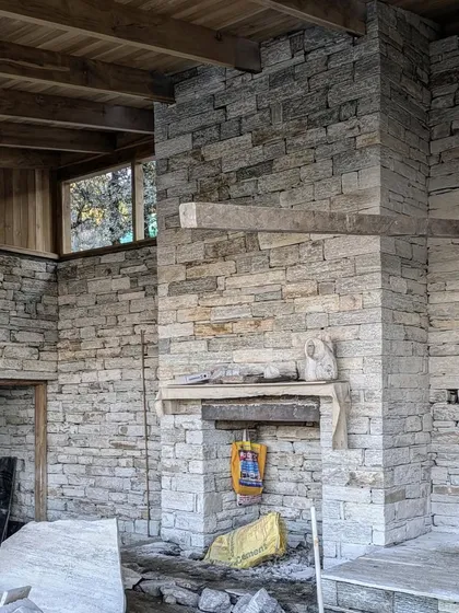 The interior stone walls and fireplace of a Himalayan guesthouse take shape. The massive stone chimney serves as the thermal heart of the home, providing warmth while anchoring the living space.