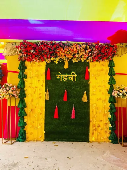A close-up of the green turf and yellow drape backdrop for a Mehndi ceremony. The bright red and yellow tassels add a beautiful contrast.