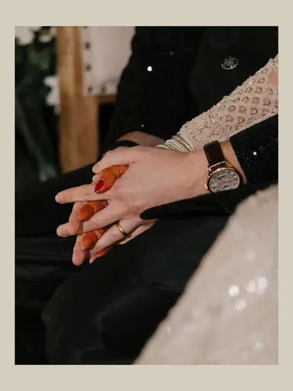 A close-up shot focusing on the couple's intertwined hands. The bride's henna-adorned hand resting on the groom's shows their connection and the beautiful details of their union.