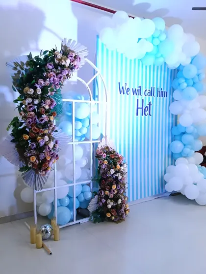 A similar naming ceremony setup to announce the name "Het". This design uses a window-frame prop and floral arrangements to add a touch of elegance to the blue and white balloon decoration.