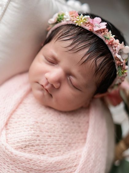 A close-up of a newborn's sweet face, framed by a pink floral headband.