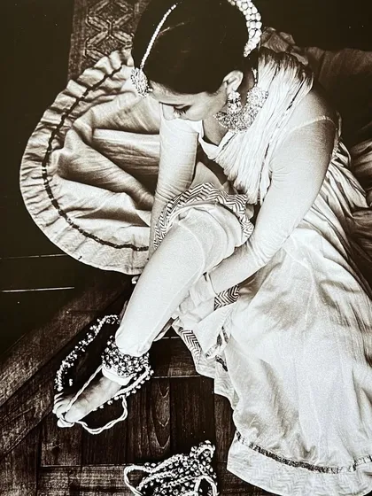 An overhead shot of me fastening my ghungroos (ankle bells), a classic ritual for a Kathak dancer, captured in a timeless black and white style.