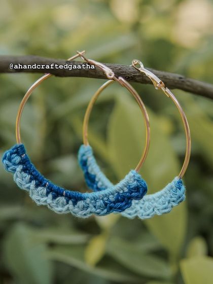 A close-up of the blue hoops hanging from a branch. The detail of the crochet work is what makes these handmade pieces so special.