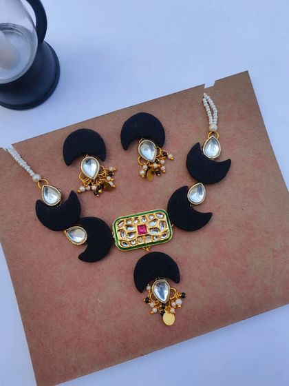This black fabric and Kundan necklace set is a modern choice for a wedding reception or sangeet. The half-moon fabric pieces are paired with a central Kundan pendant and matching earrings.