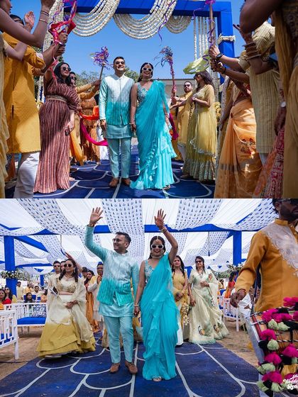 The grand entrance of the bride and groom at their Haldi event, waving to guests as they walk down a vibrant blue aisle.